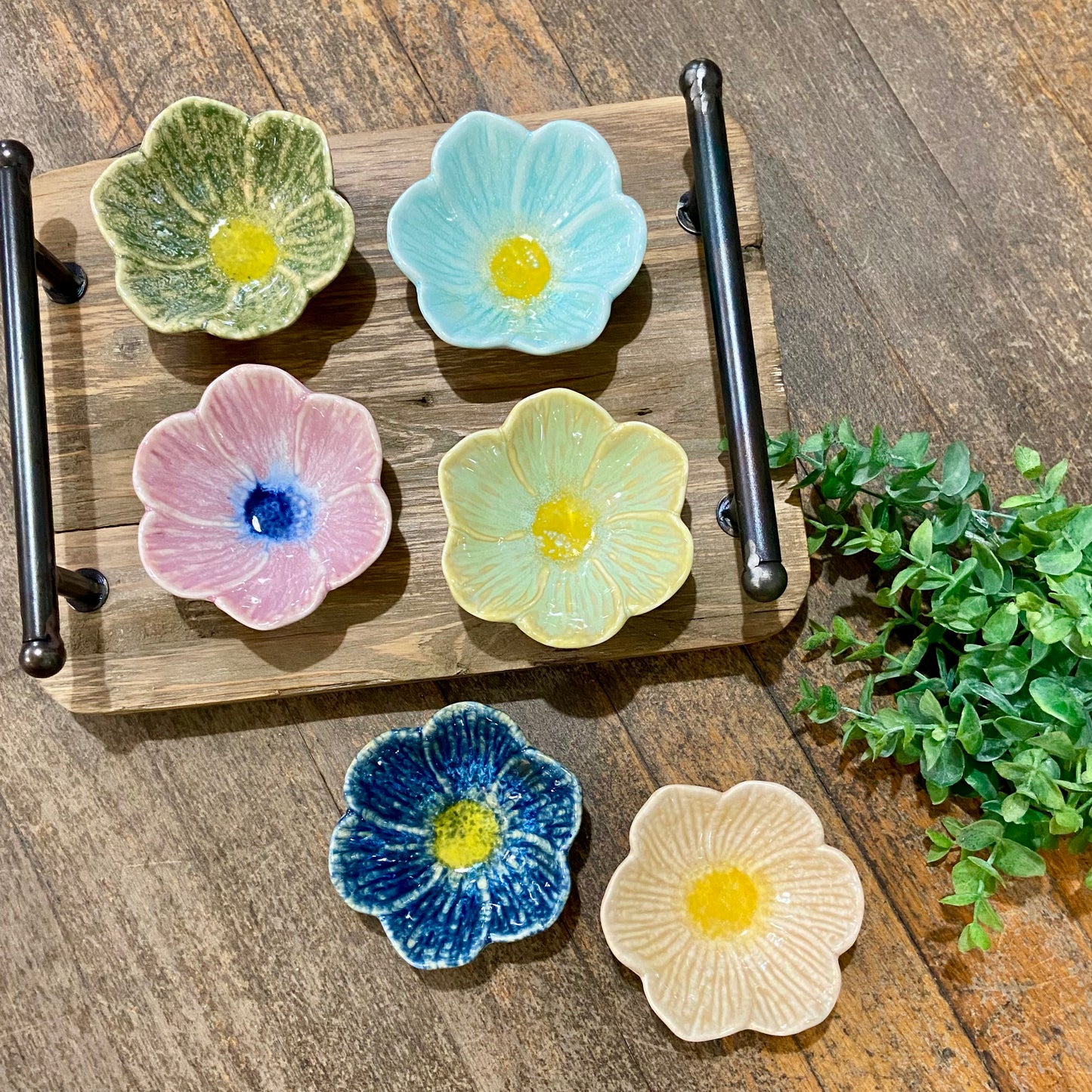 Set of colorful ceramic flower-shaped dishes on a wooden board with a plant in the background.