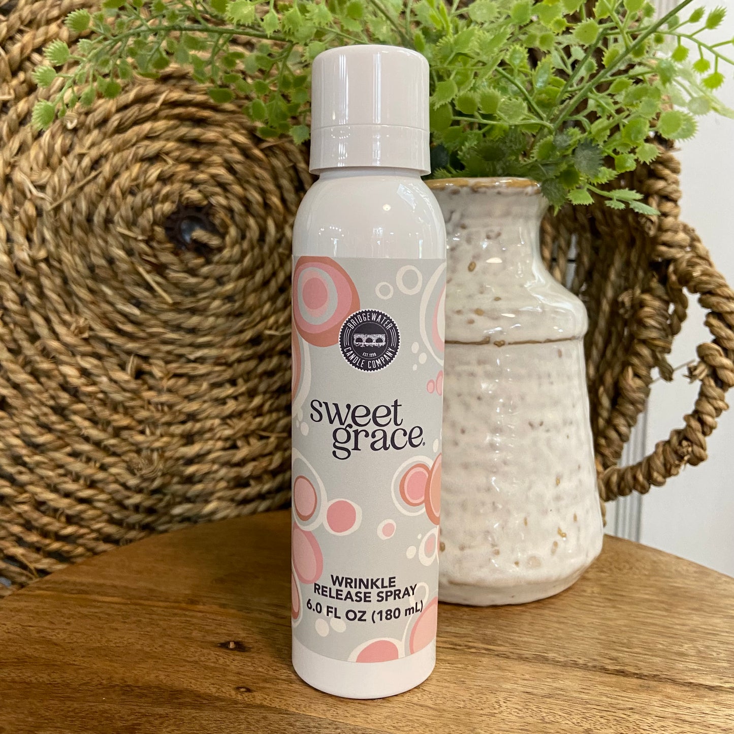 Sweet Grace wrinkle release spray bottle on a wooden surface with a vase and plants in the background