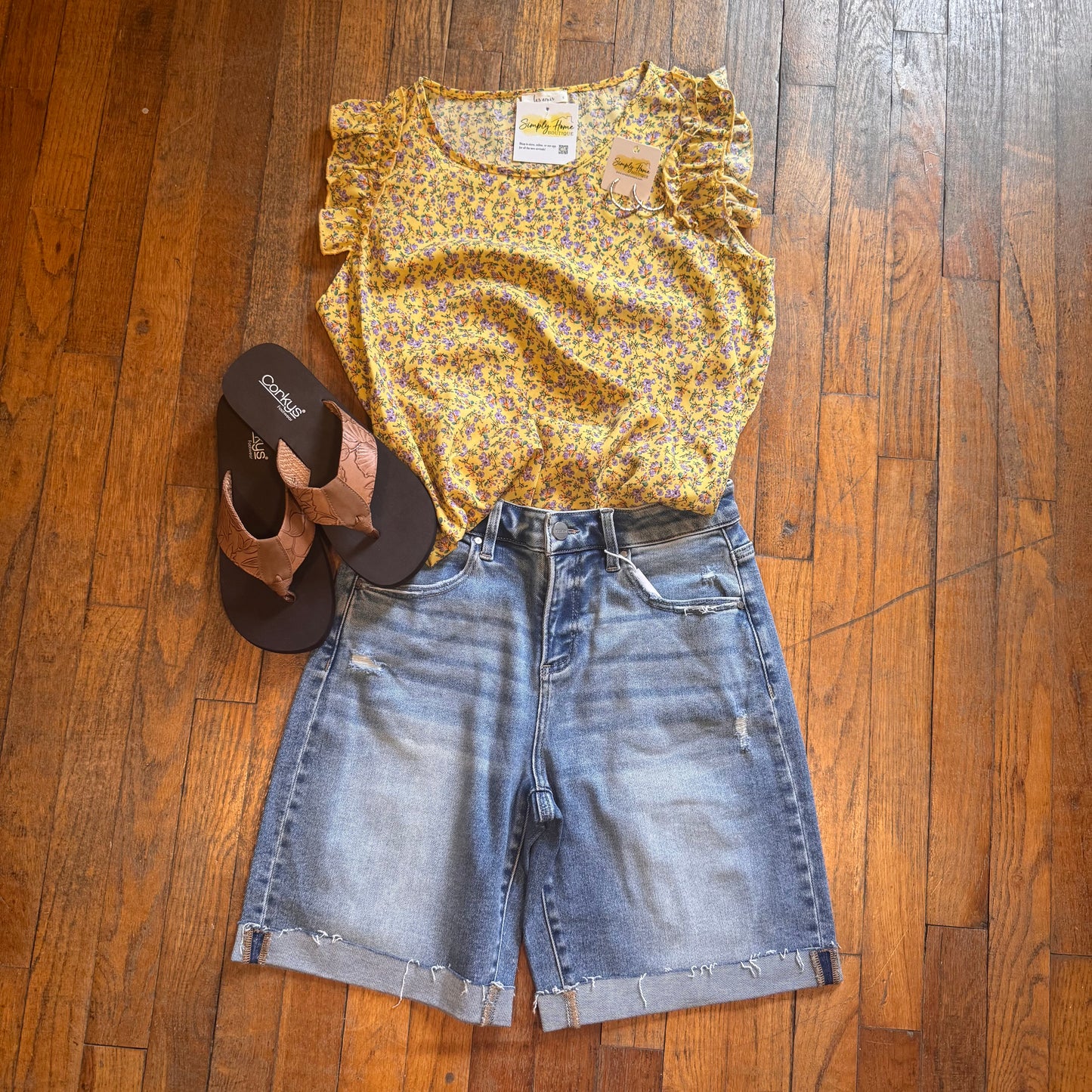 Yellow floral top and blue denim shorts with brown sandals on a wooden floor