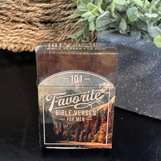 Box of '101 Favorite Bible Verses for Men' on a dark surface with a woven mat and plant in the background.