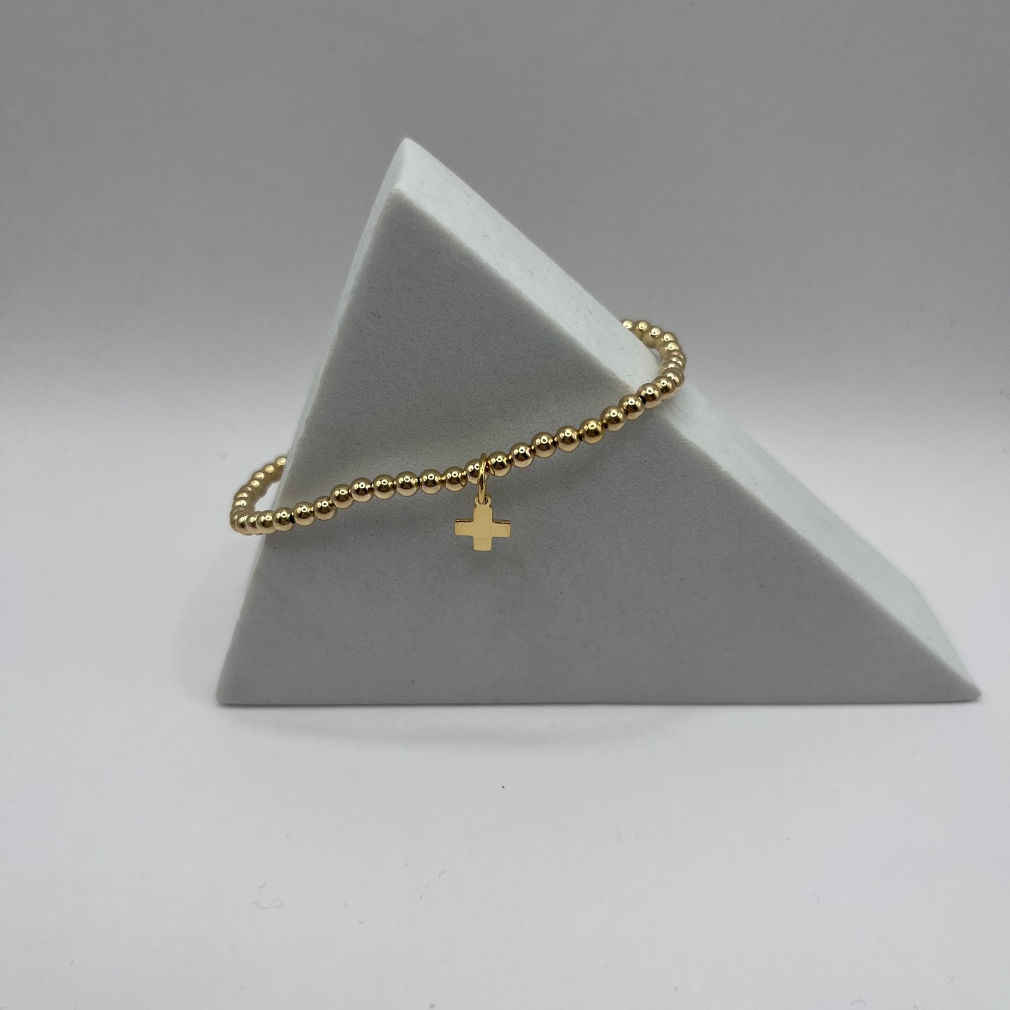 Gold bracelet with a cross charm on a gray triangular stand