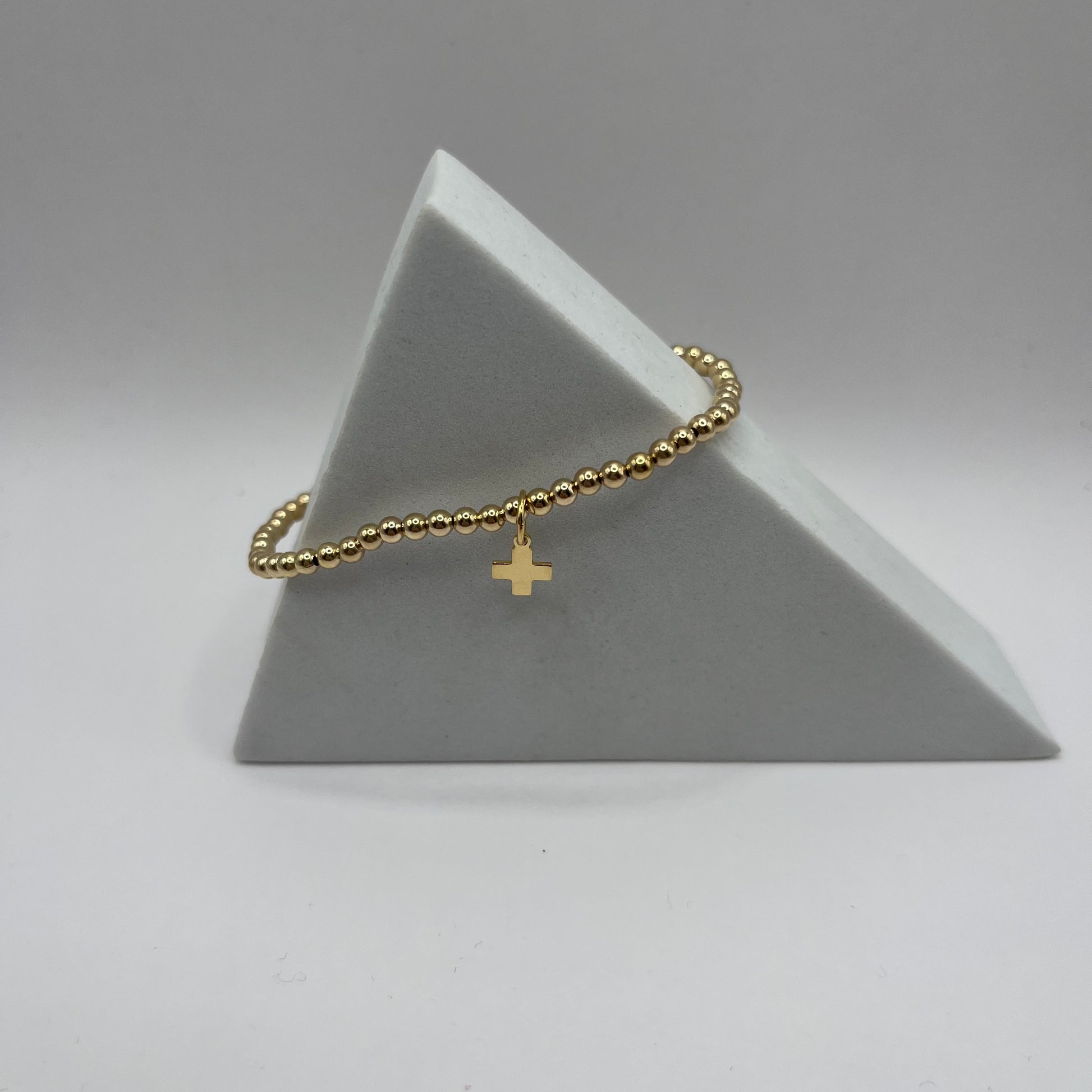 Gold bracelet with a cross charm on a gray triangular stand