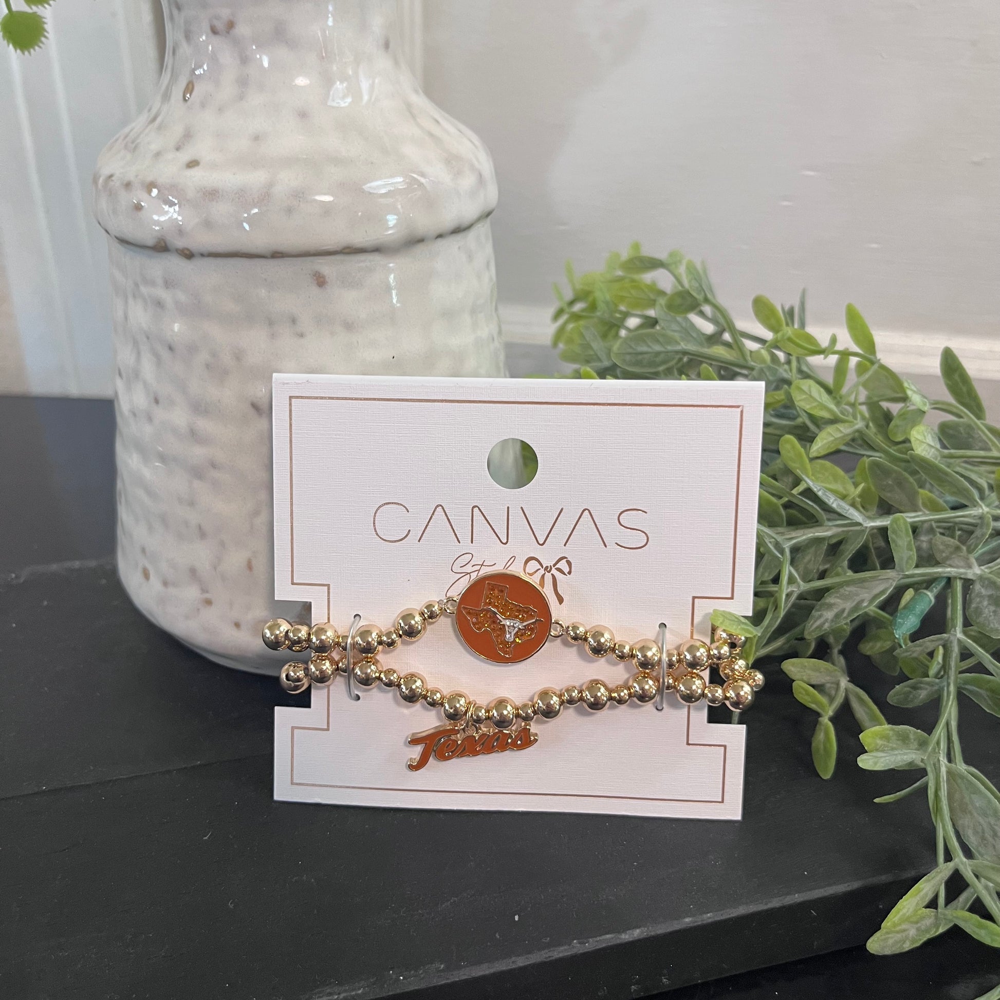 Gold bracelet on a 'Canvas' branded card with a vase and plant in the background