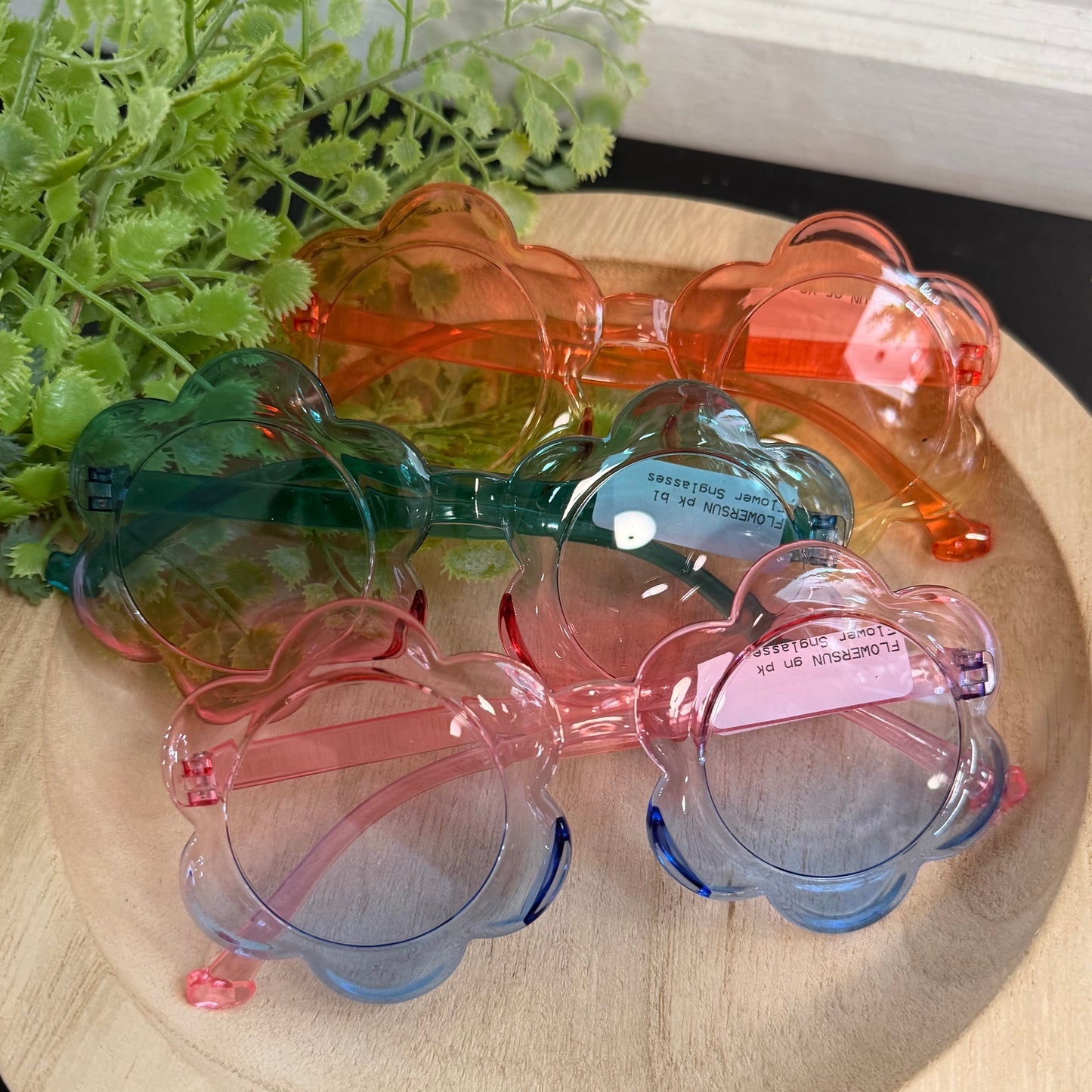 Set of colorful sunglasses on a wooden surface with greenery in the background