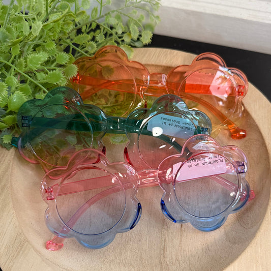 Set of colorful sunglasses on a wooden surface with greenery in the background