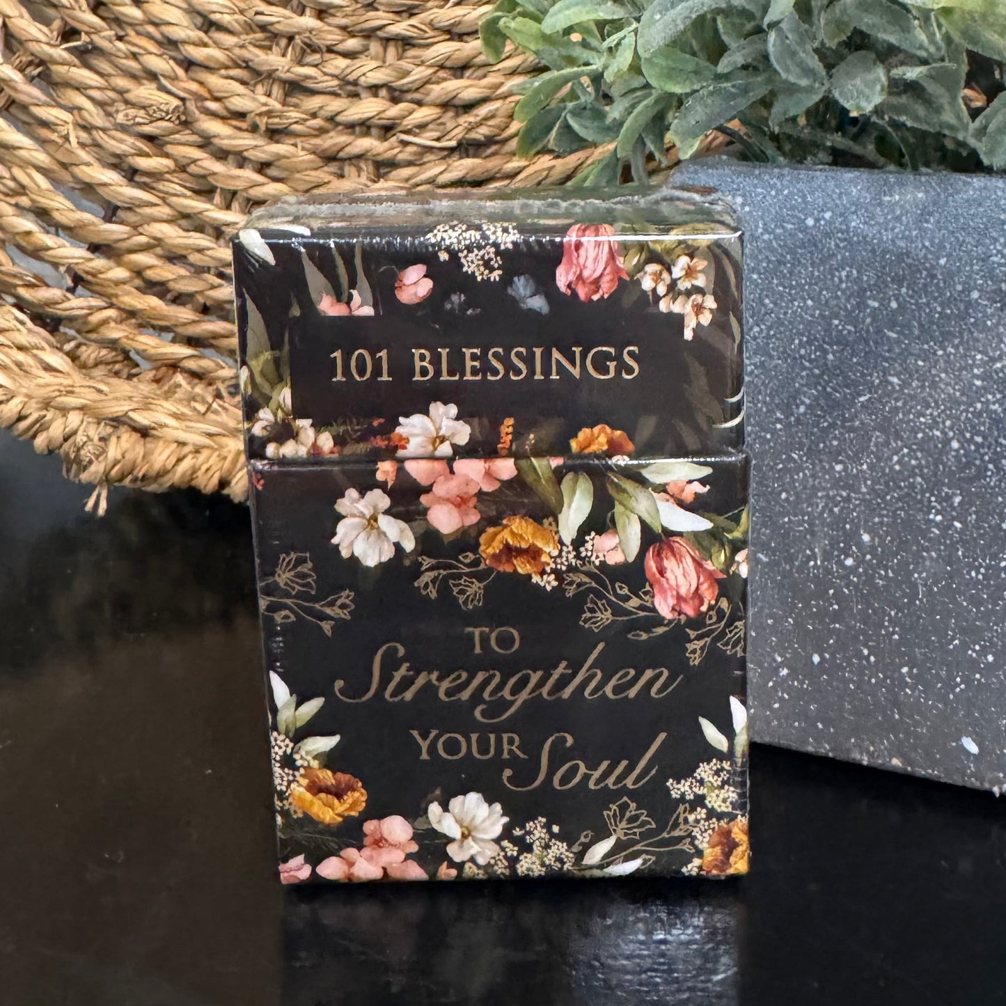 Small book titled '101 Blessings to Strengthen Your Soul' with floral design on a dark surface.