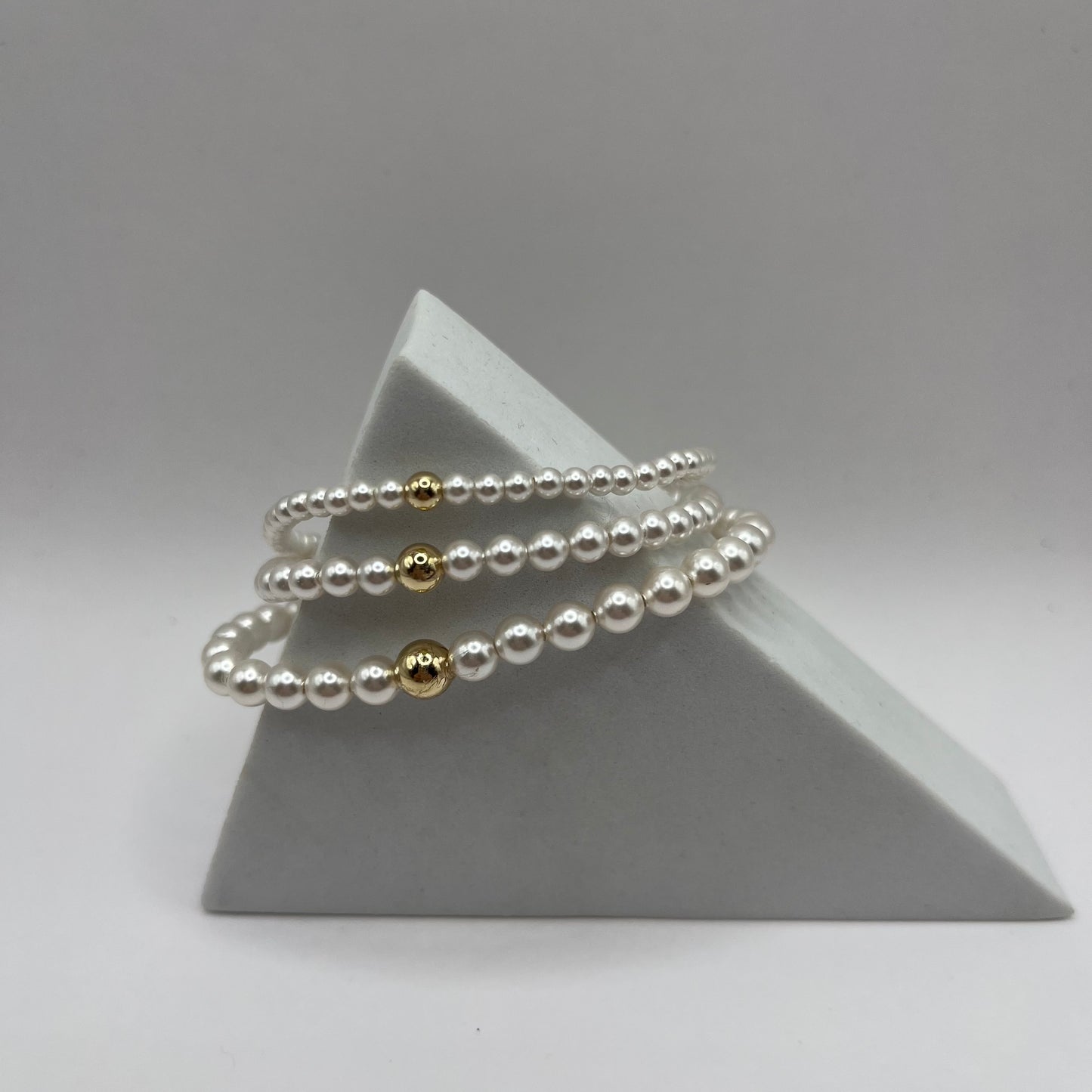 Set of pearl bracelets with gold accents on a gray pyramid stand