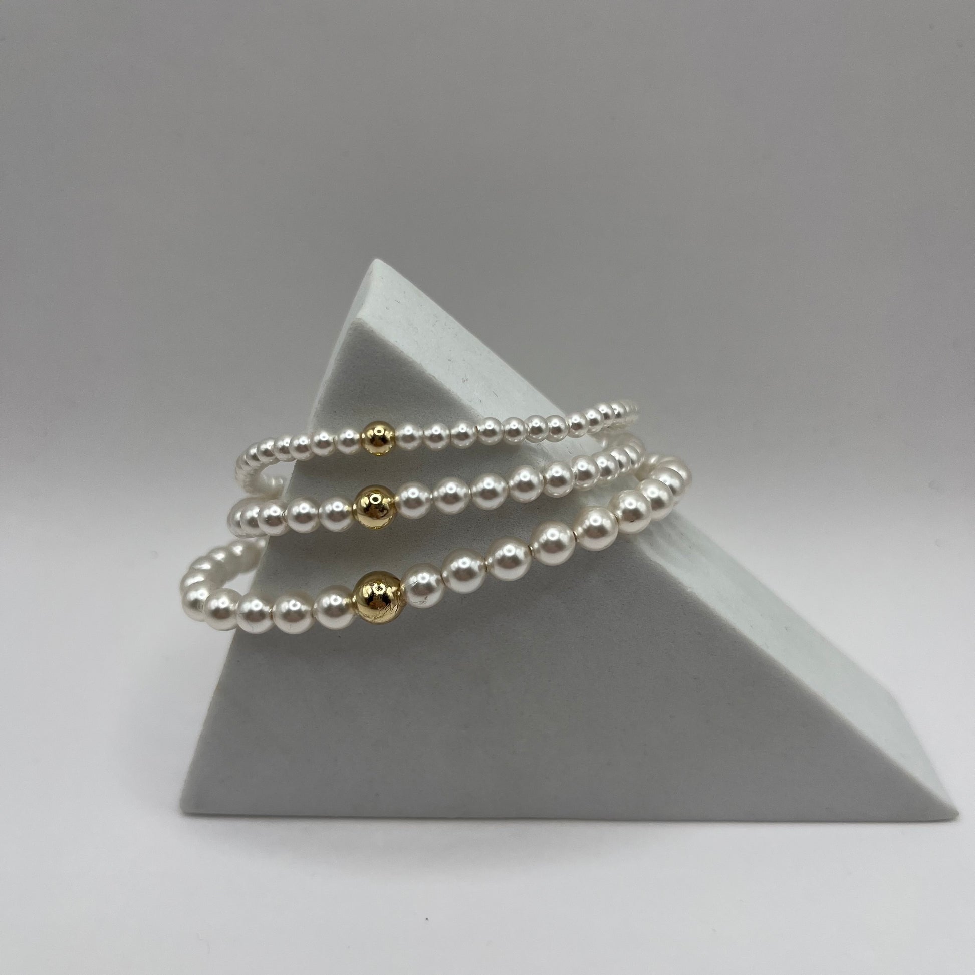Set of pearl bracelets with gold accents on a gray pyramid stand