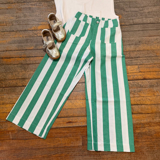 Green and white striped pants with a beige sleeveless top and shoes on a wooden surface