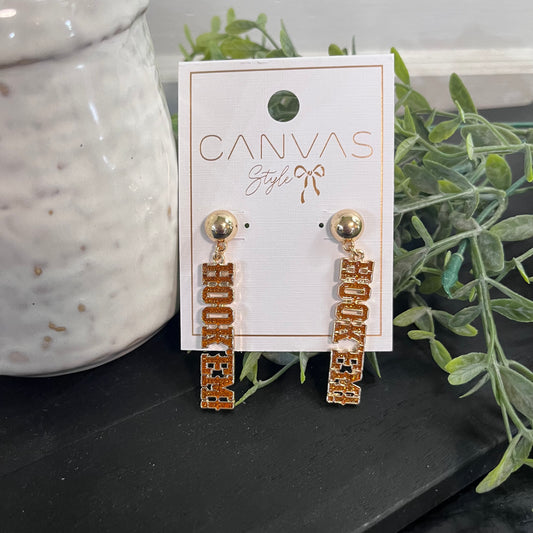 Gold earrings on a 'Canvas Style' branded card with greenery in the background