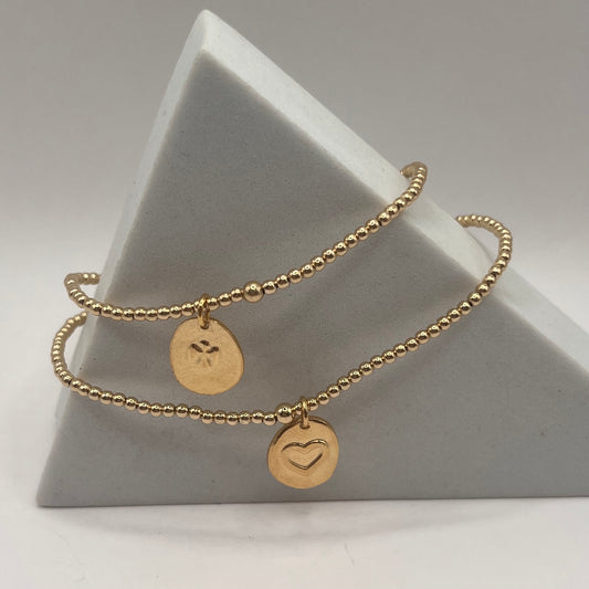 Gold bracelet with heart and leaf charms on a gray triangular stand