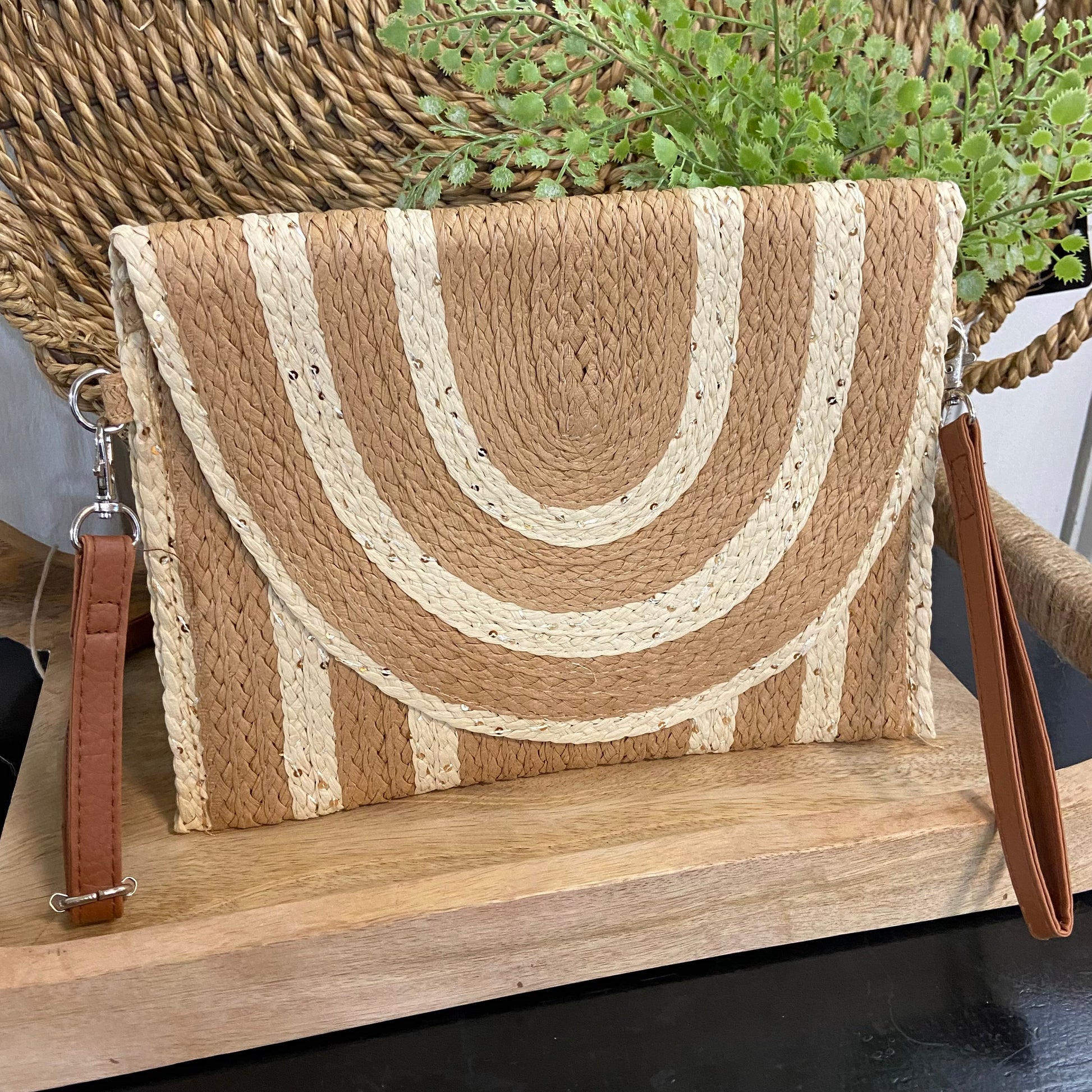 Woven clutch bag with a brown strap on a wooden surface