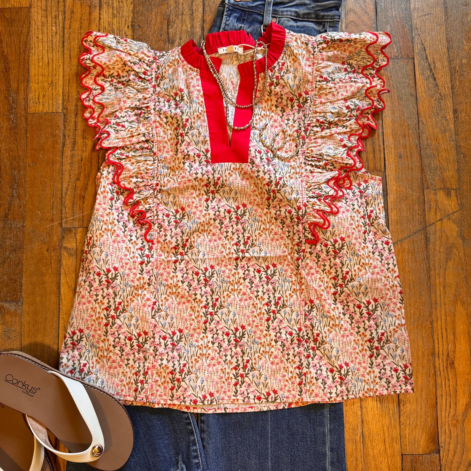 Floral top with red trim and denim shorts on a wooden floor