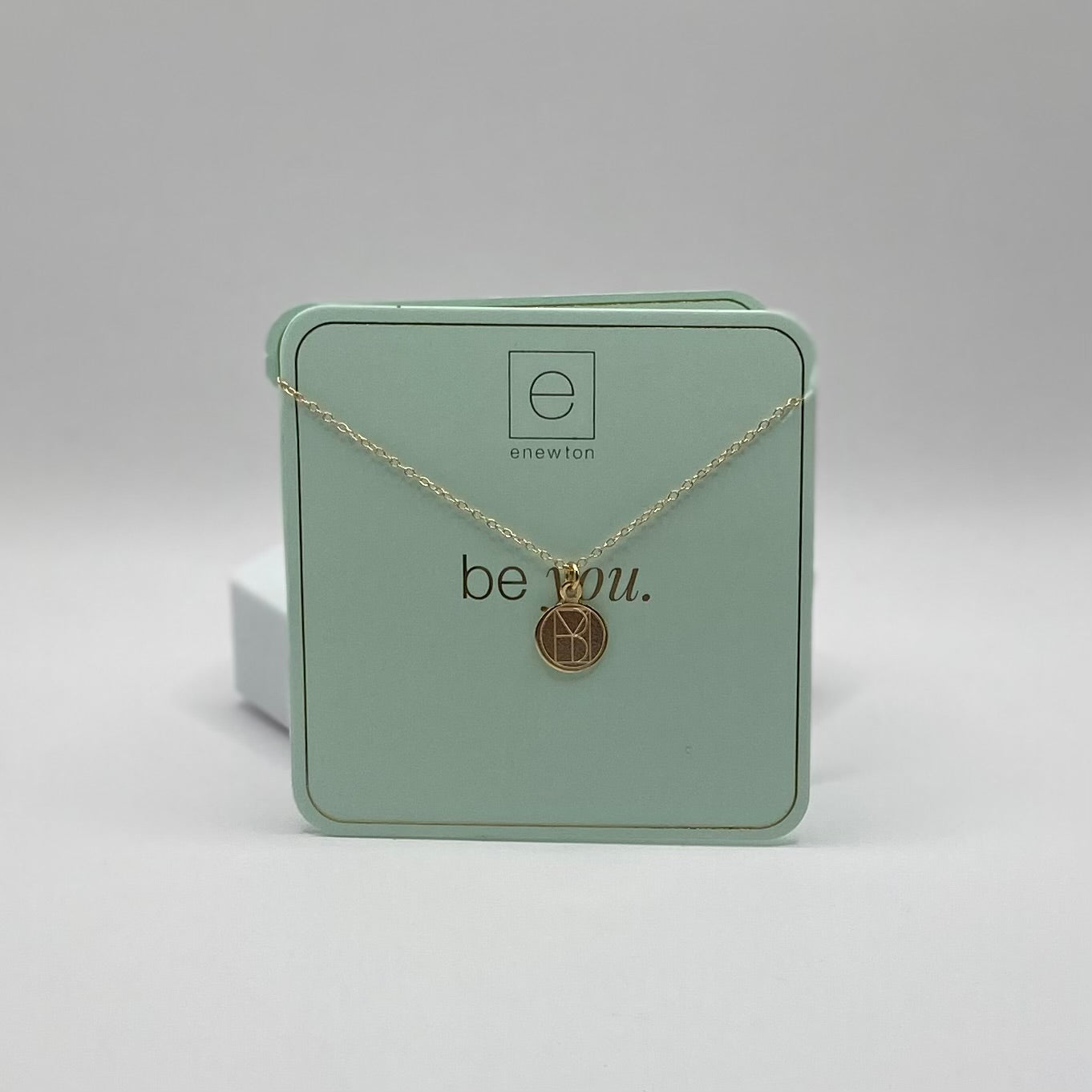 Gold necklace with a pendant on a green box labeled 'be you.'