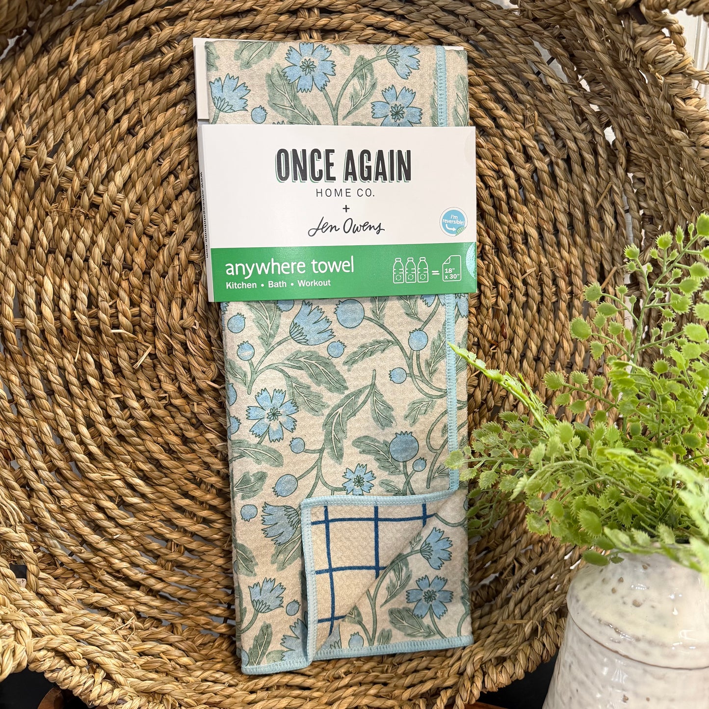 Packaged 'Anywhere Towel' with floral design on a woven surface