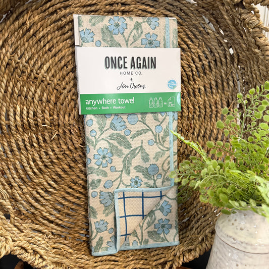Packaged 'Anywhere Towel' with floral design on a woven surface