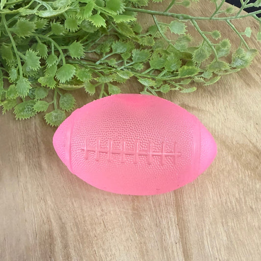 Pink textured object on a wooden surface with green leaves in the background