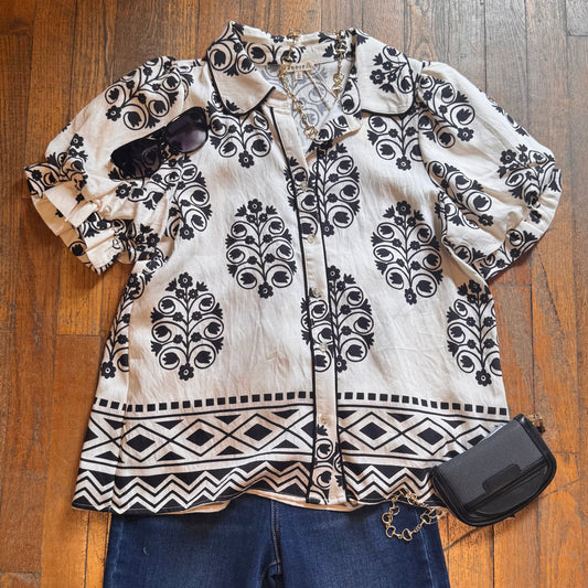 Black and white patterned blouse with blue jeans and a black handbag on a wooden floor.