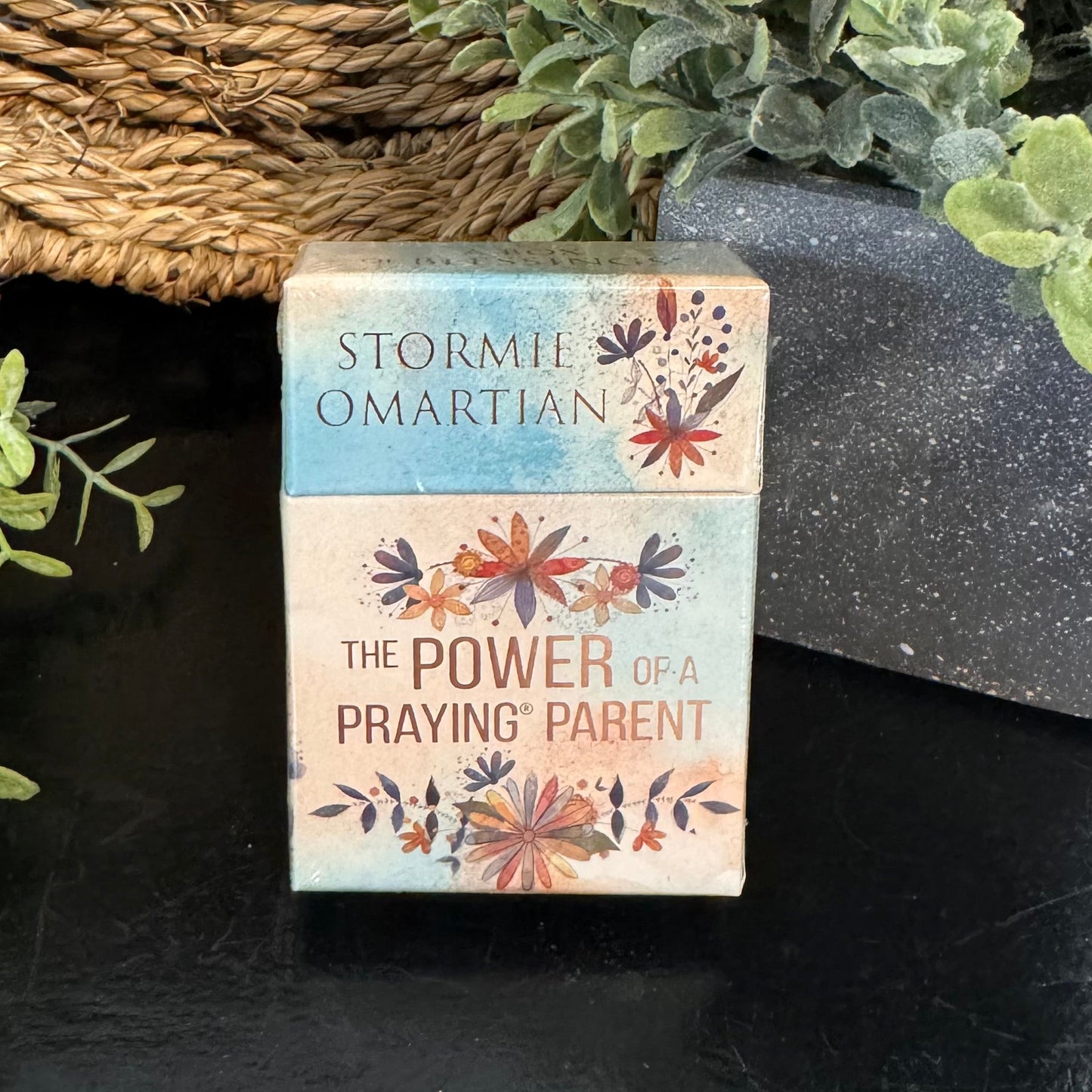 Book titled 'The Power of a Praying Parent' by Stormie Omartian on a dark surface with plants in the background.