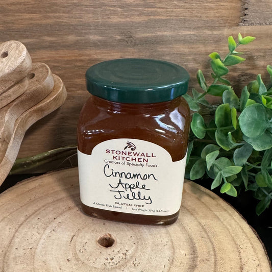 Jar of Stonewall Kitchen Cinnamon Apple Jelly on a wooden surface with a wooden cutting board and plant in the background.