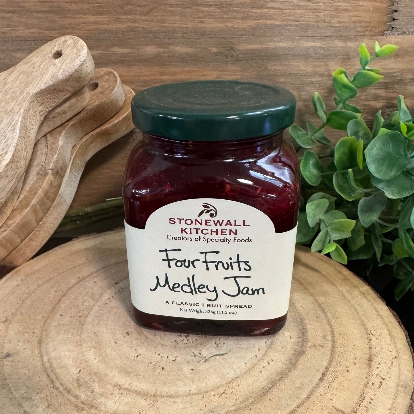 Jar of Stonewall Kitchen Four Fruits Medley Jam on a wooden surface with a plant in the background