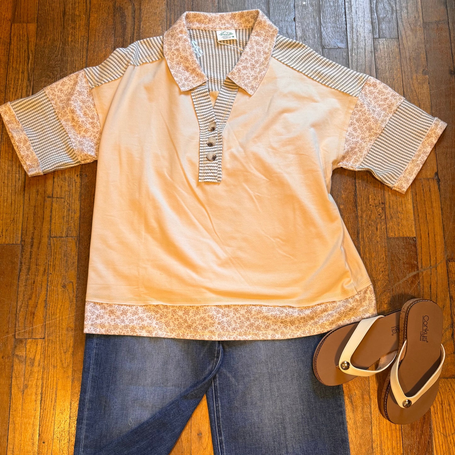 Beige polo shirt with lace details, blue jeans, and brown sandals on a wooden floor.