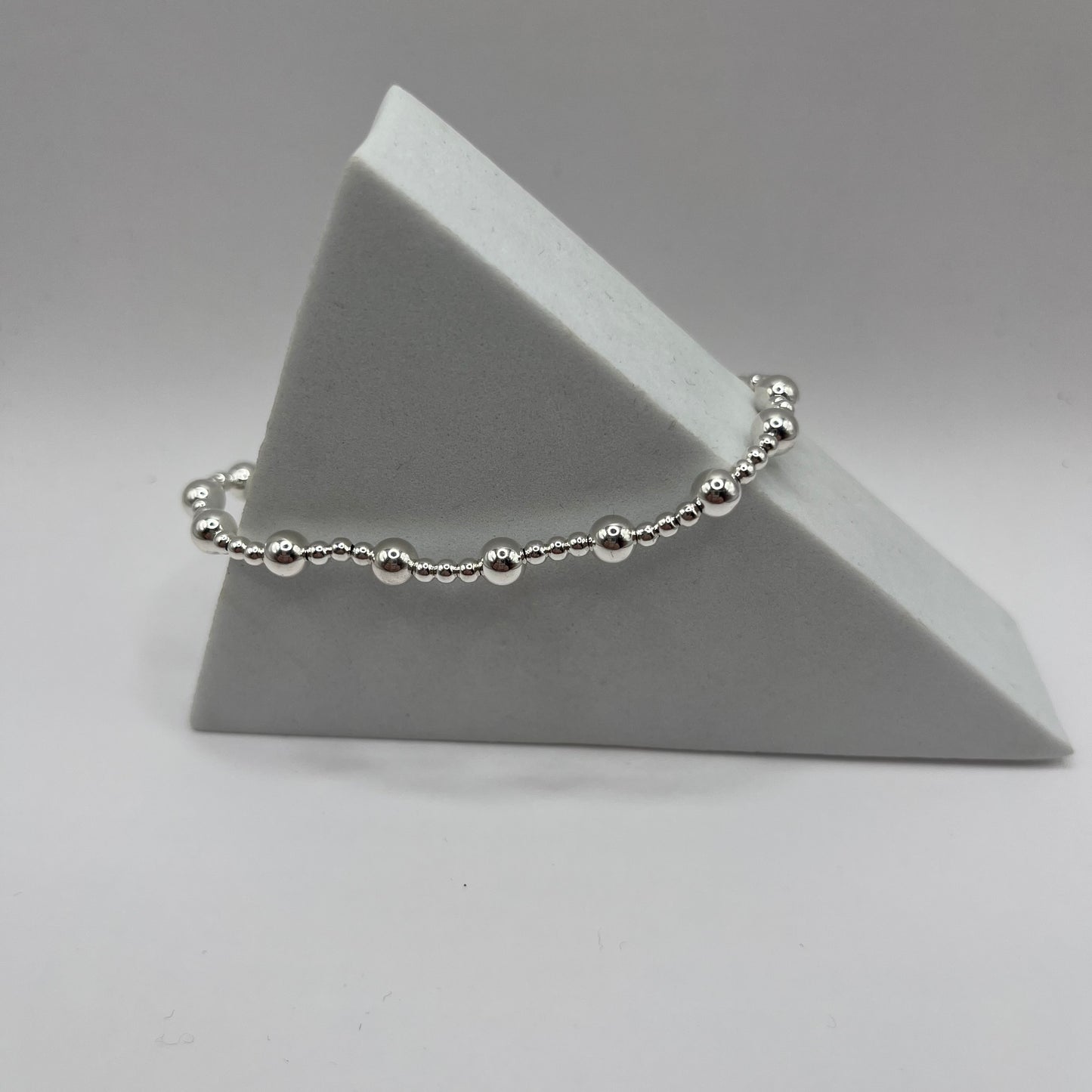 Silver beaded bracelet on a gray triangular stand against a gray background