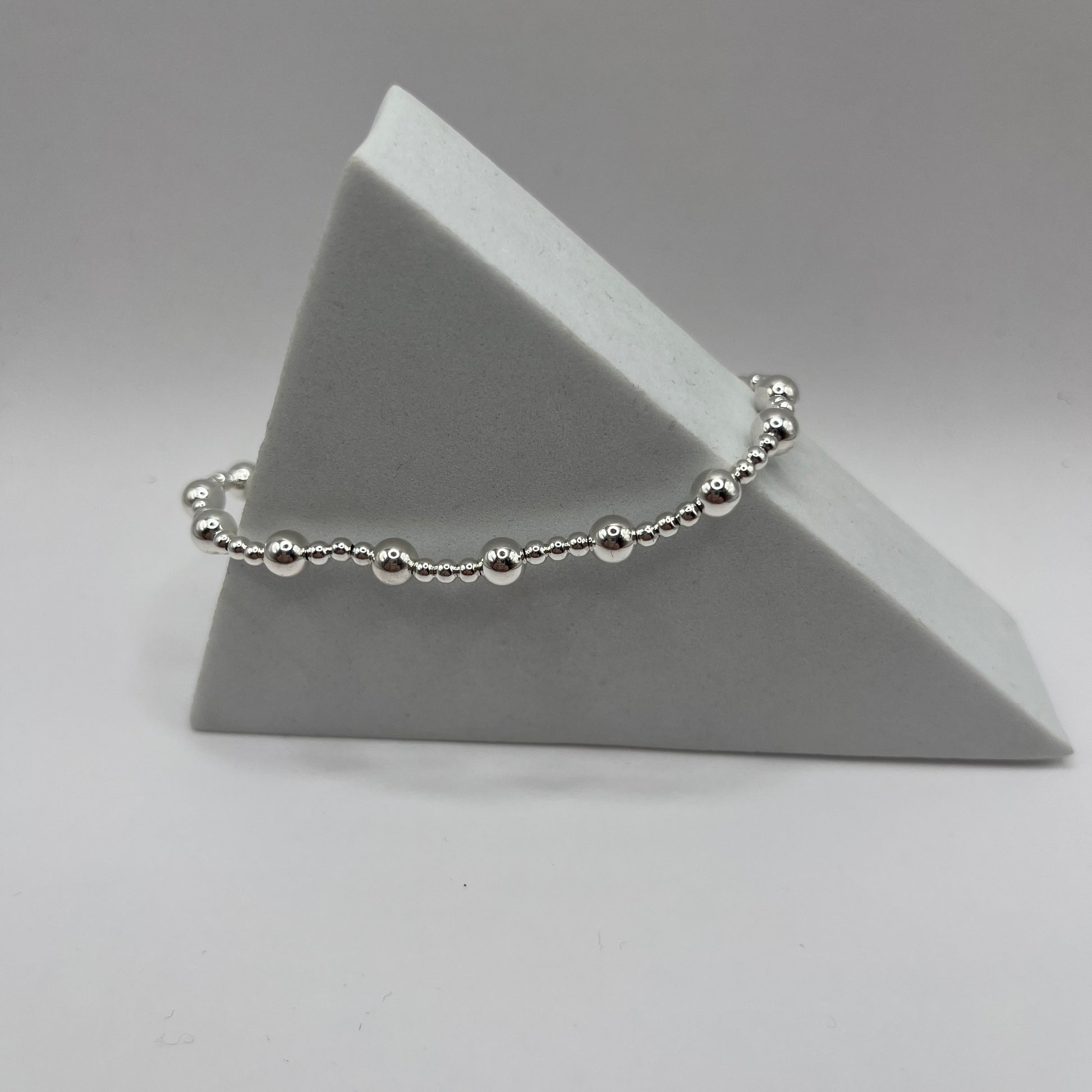 Silver beaded bracelet on a gray triangular stand against a gray background