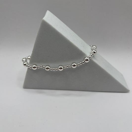 Silver beaded bracelet on a gray triangular stand against a gray background