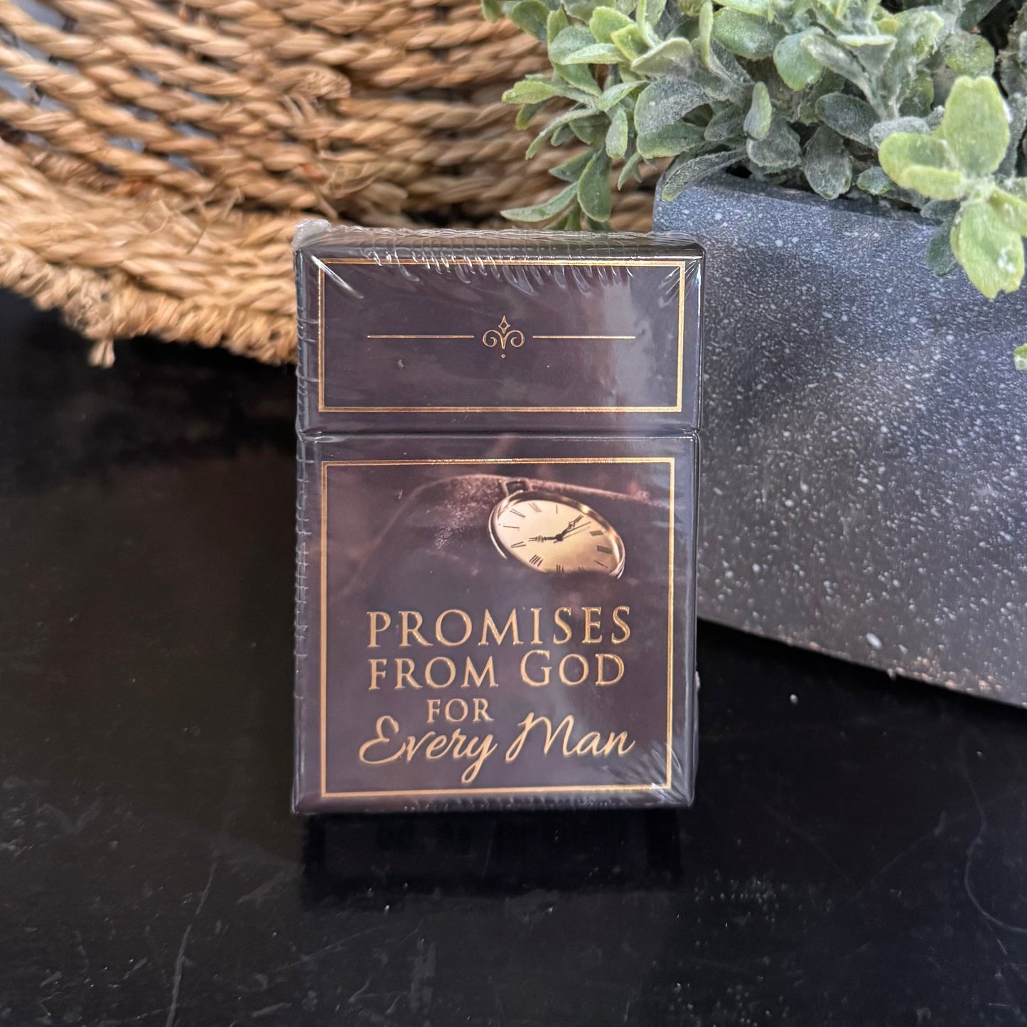 Book titled 'Promises from God for Every Man' next to a potted plant on a dark surface with a woven mat in the background.