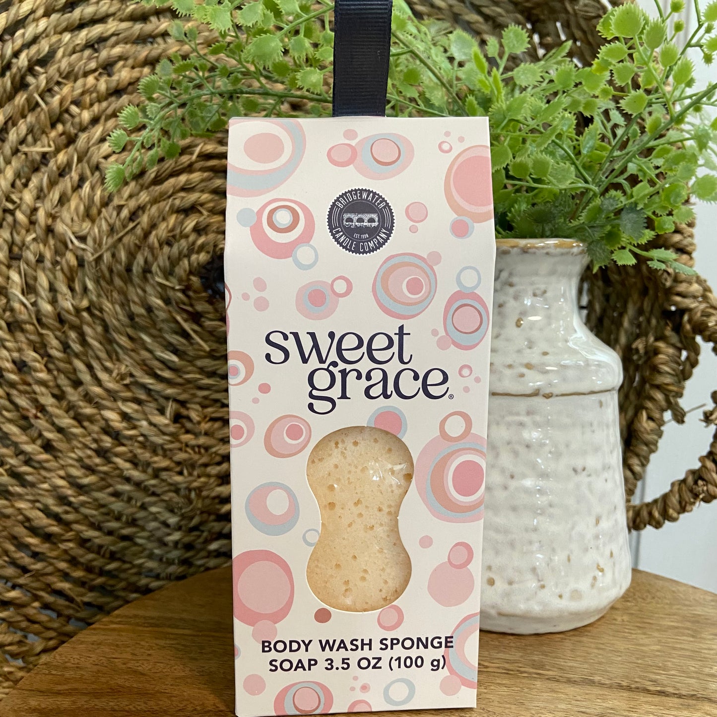 Box of 'sweet grace' body wash sponge with decorative elements on a wooden surface.