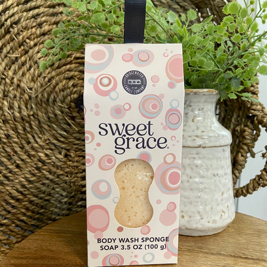 Box of 'sweet grace' body wash sponge with decorative elements on a wooden surface.