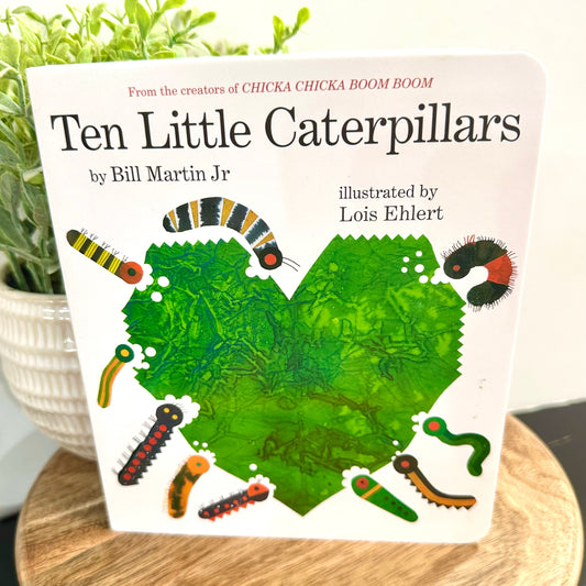Book titled 'Ten Little Caterpillars' by Bill Martin Jr. on a wooden surface with a plant in the background.