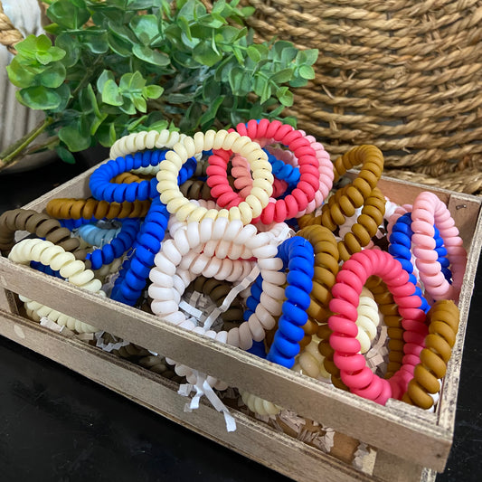 Colorful spiral hair ties in a wooden box with a plant in the background