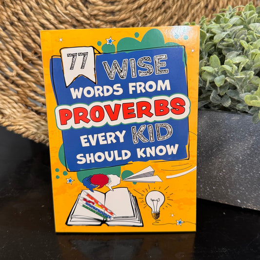 Book titled '77 Wise Words from Proverbs Every Kid Should Know' on a dark surface with a plant in the background.