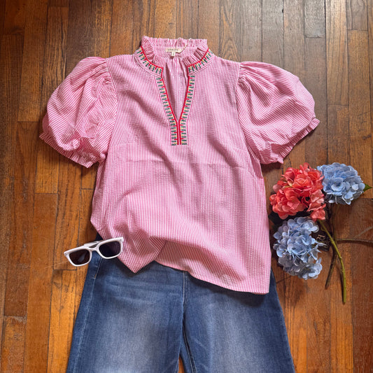 Pink outfit with blue jeans, sunglasses, and flowers on a wooden floor