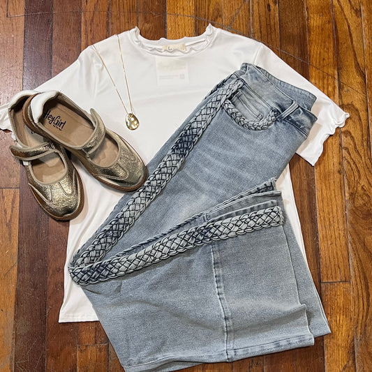 White shirt, blue jeans with braided details, and brown shoes on a wooden floor.
