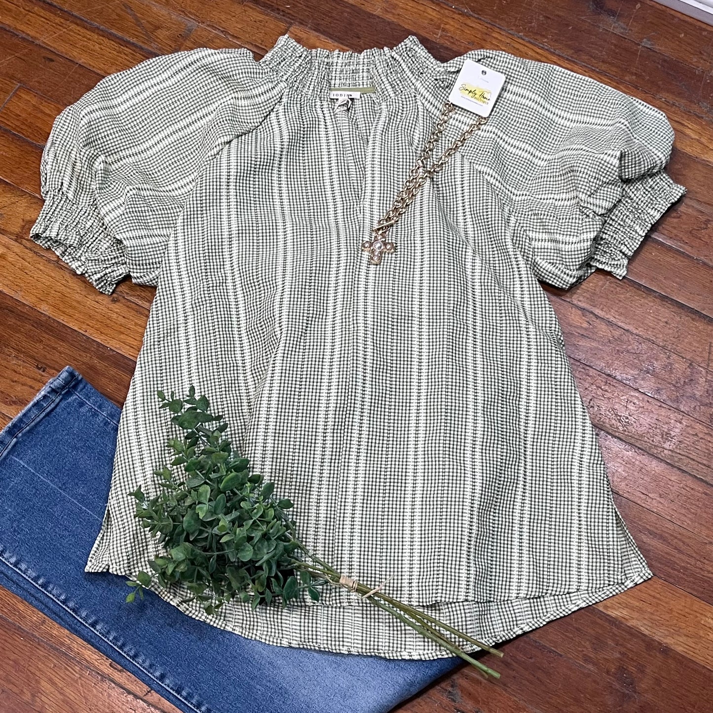 Checkered blouse with ruffled sleeves on a wooden floor with jeans and a plant.