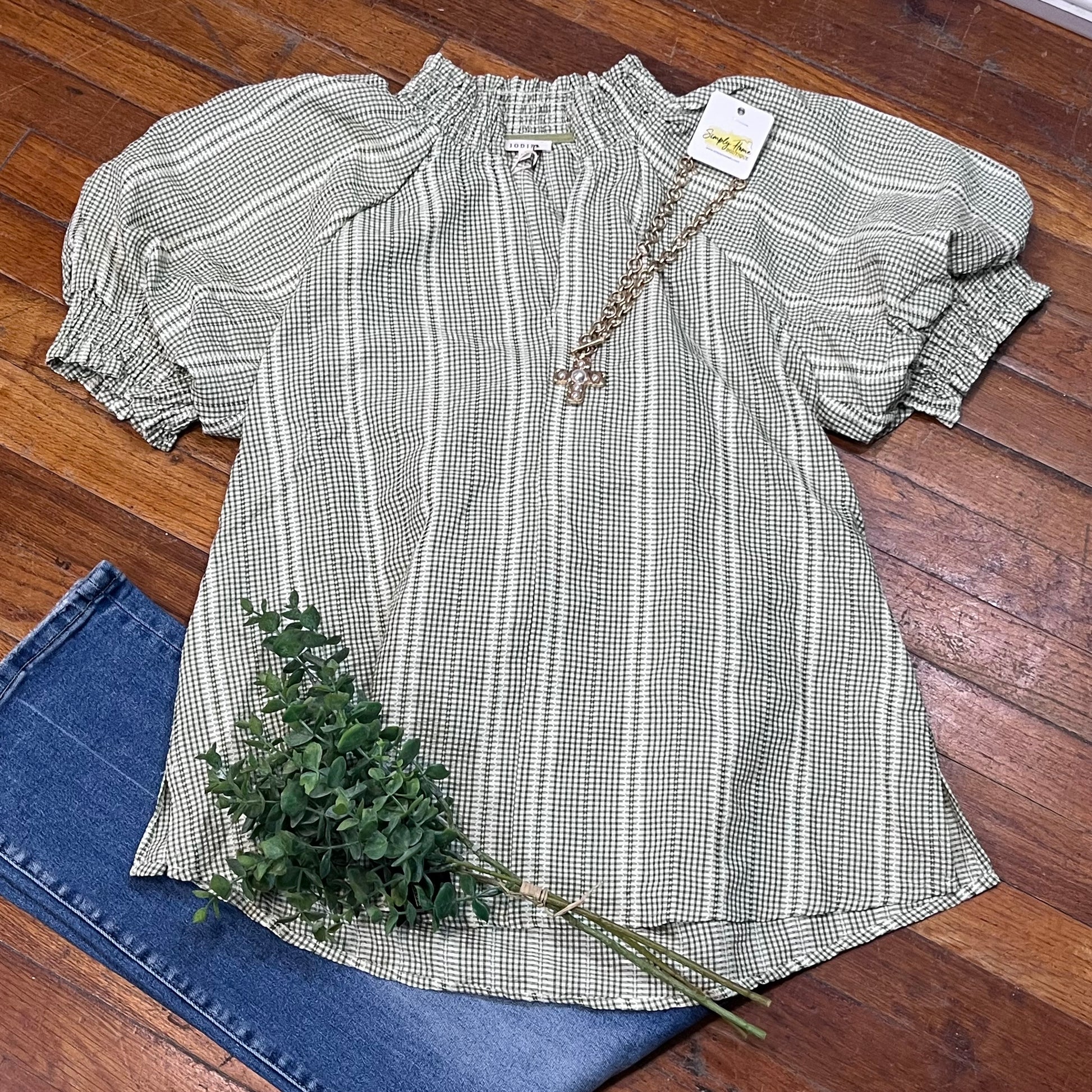 Checkered blouse with ruffled sleeves on a wooden floor with jeans and a plant.