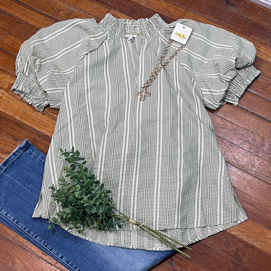 Checkered blouse with ruffled sleeves on a wooden floor with jeans and a plant.