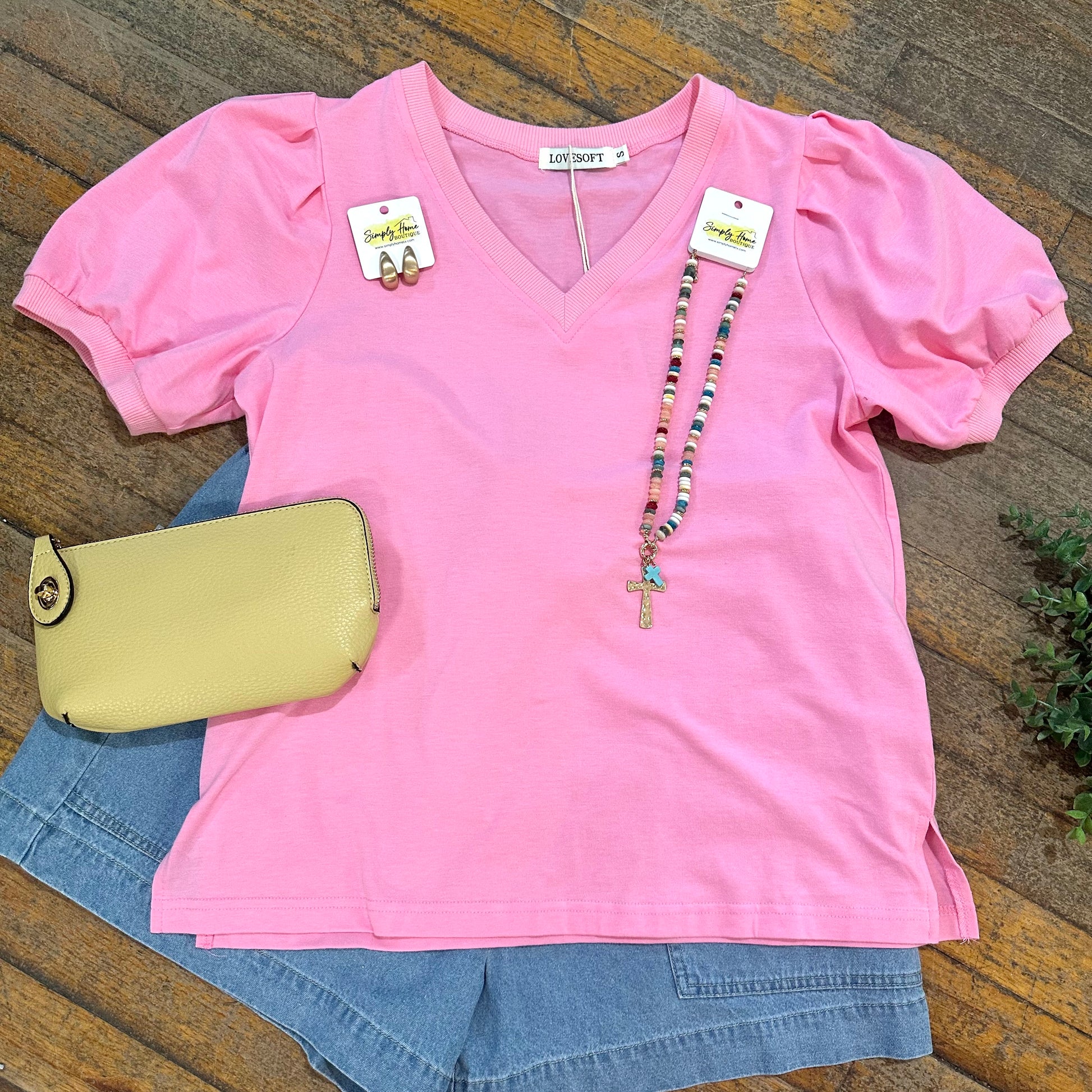 Pink top with denim shorts and a yellow purse on a wooden surface