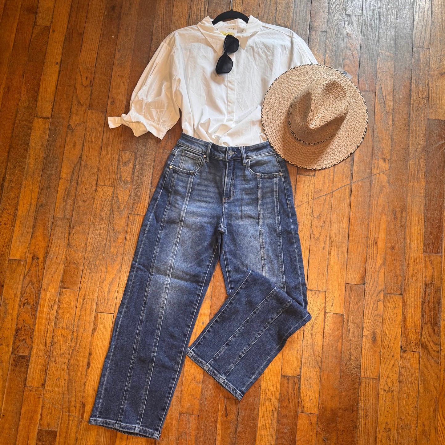 White blouse, blue jeans, and straw hat on a wooden floor