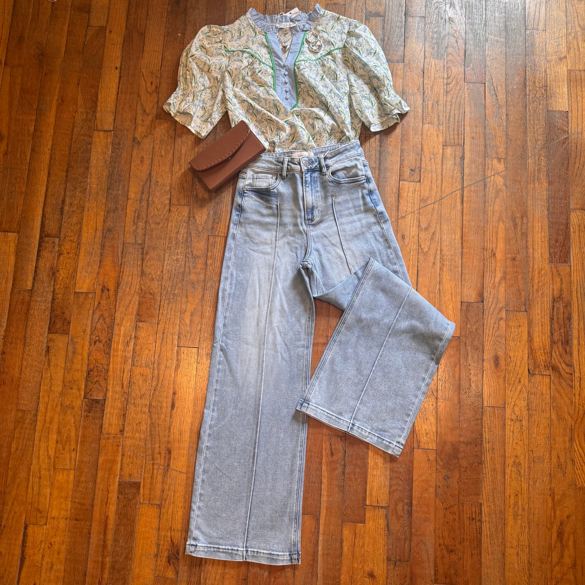 Top, jeans, and brown clutch on a wooden floor