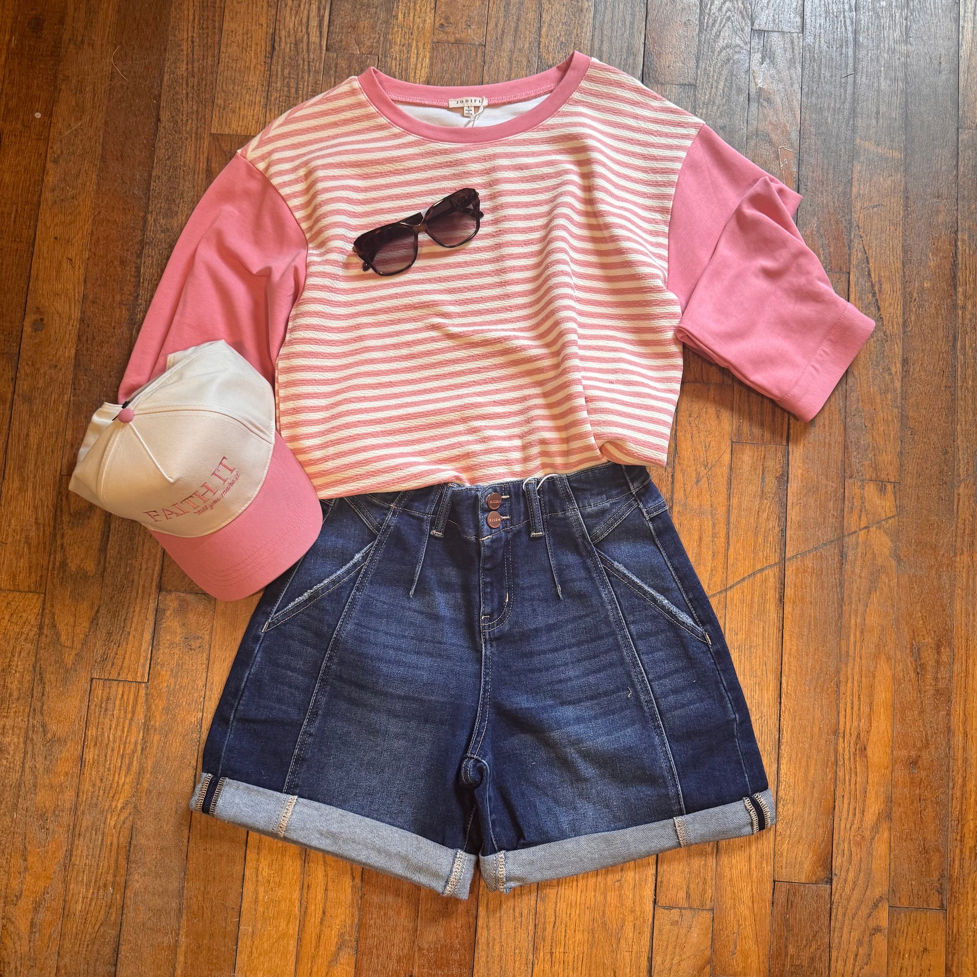 Pink and white striped shirt with sunglasses and denim shorts on a wooden floor