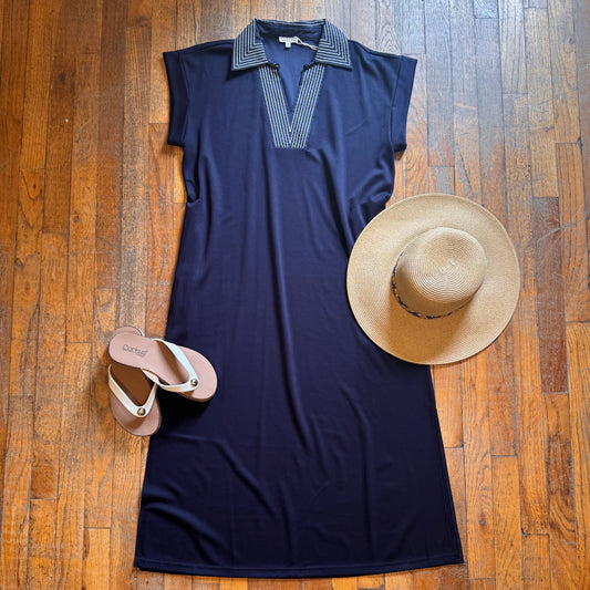 Navy sleeveless dress with striped collar, beige sandals, and straw hat on a wooden floor.