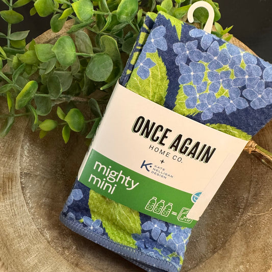 Packaged product with floral design and 'Once Again Home Co' branding on a wooden surface with greenery.