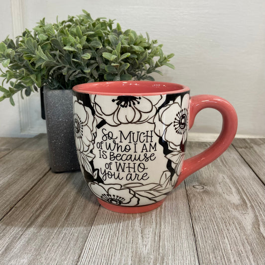 Mug with floral design and text on a wooden surface with a plant in the background