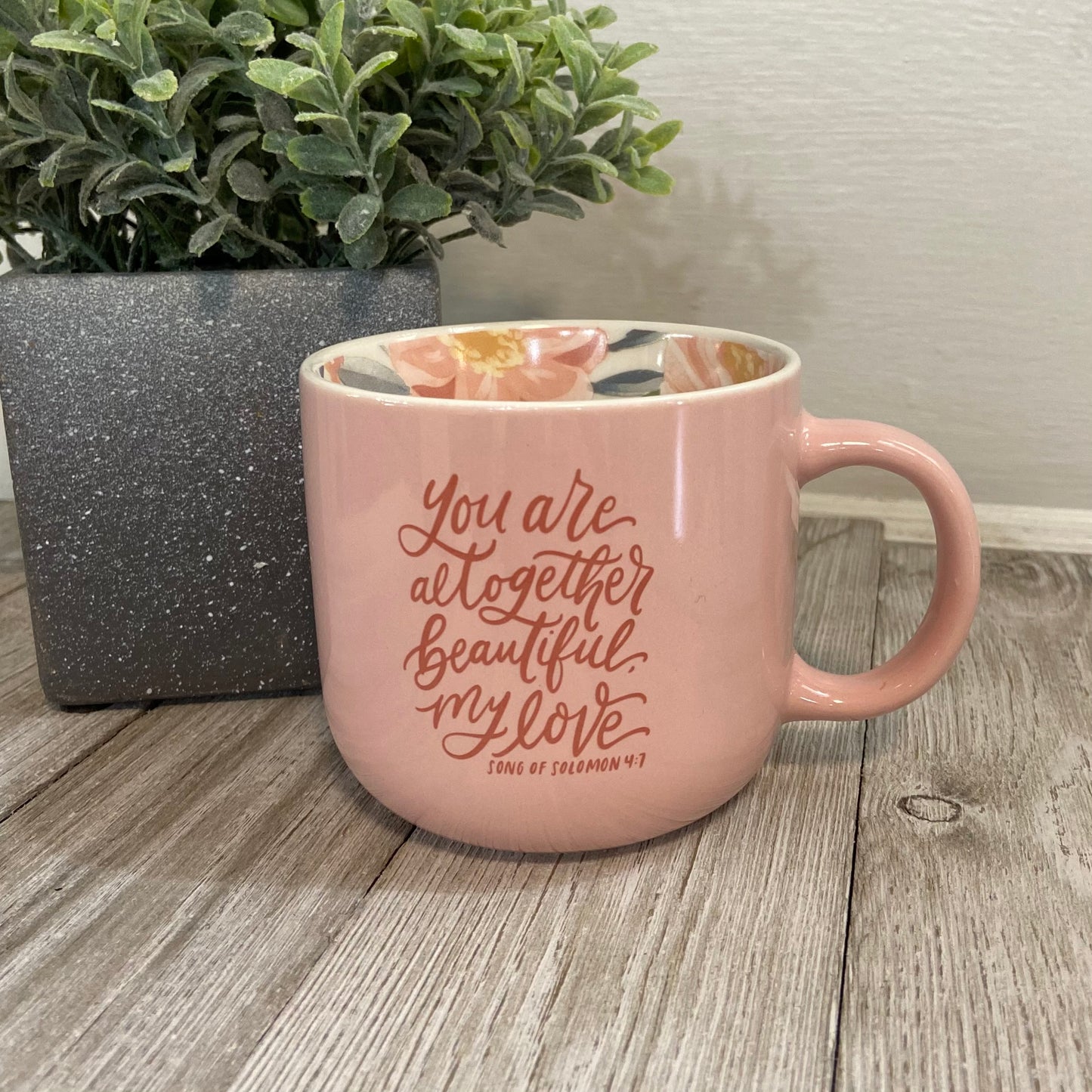 Pink mug with motivational quote on a wooden surface with a plant in the background