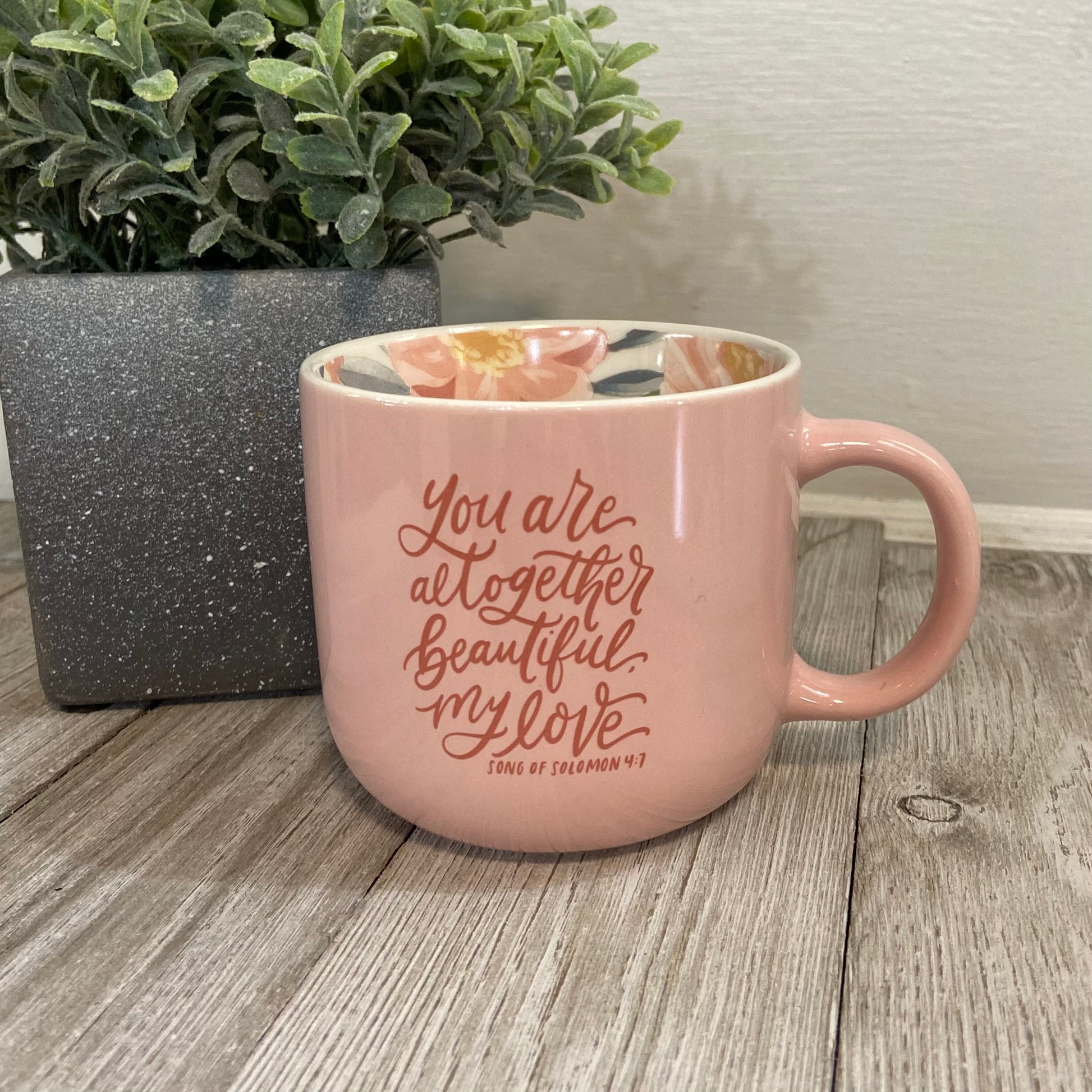 Pink mug with motivational quote on a wooden surface with a plant in the background