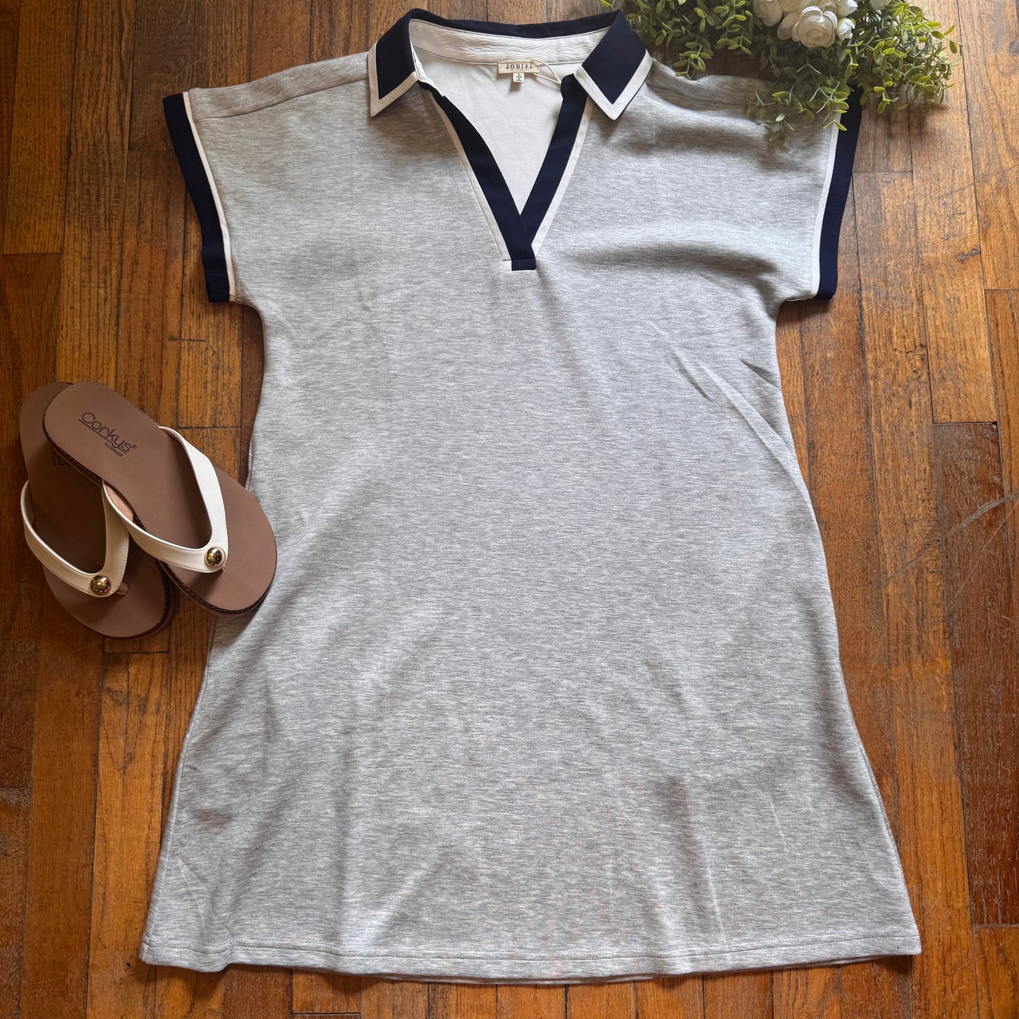 Gray sleeveless dress with black collar on a wooden floor with sandals and a plant.